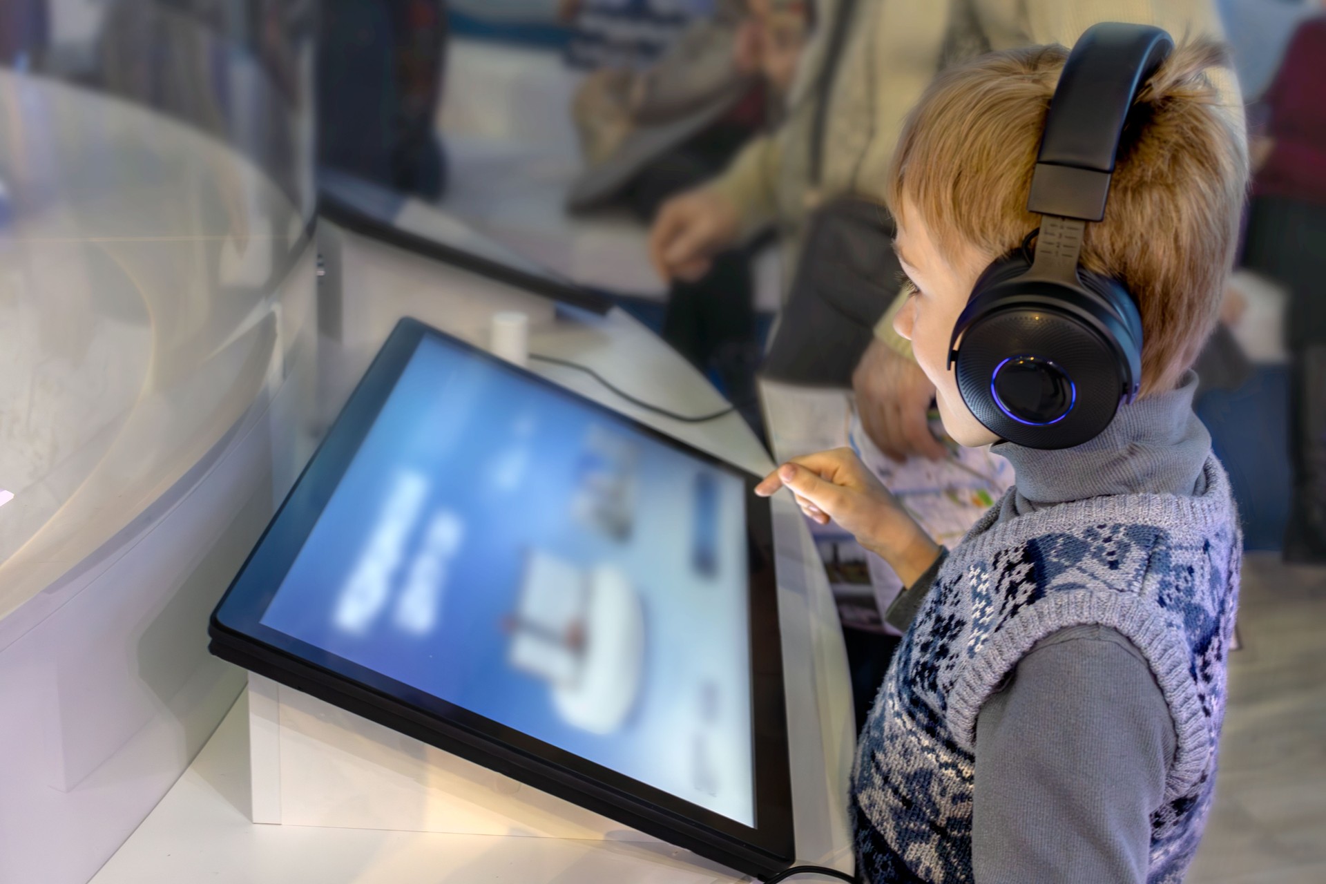 Boy wearing headphones interacts with interactive screen at an exhibit